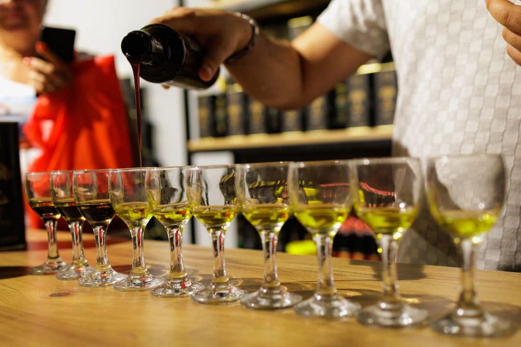 Olive oil expert pouring olive oil into a glass in a row of glasses each filled with different types of olive oil.