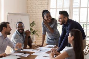 Five colleagues gathered around a table engaged in a brainstorming session together, smiling and talking.