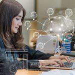 Employee sitting at a desk at a computer, with AI symbols overlaying the image, appearing to come out of the laptop.