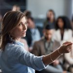 Female leader leading a leadership development training seminar in front of a large group of employees