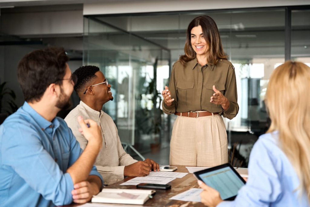 Female manager leading a team learning session, standing in front of three employees around a table