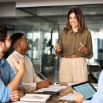 Female manager leading a team learning session, standing in front of three employees around a table