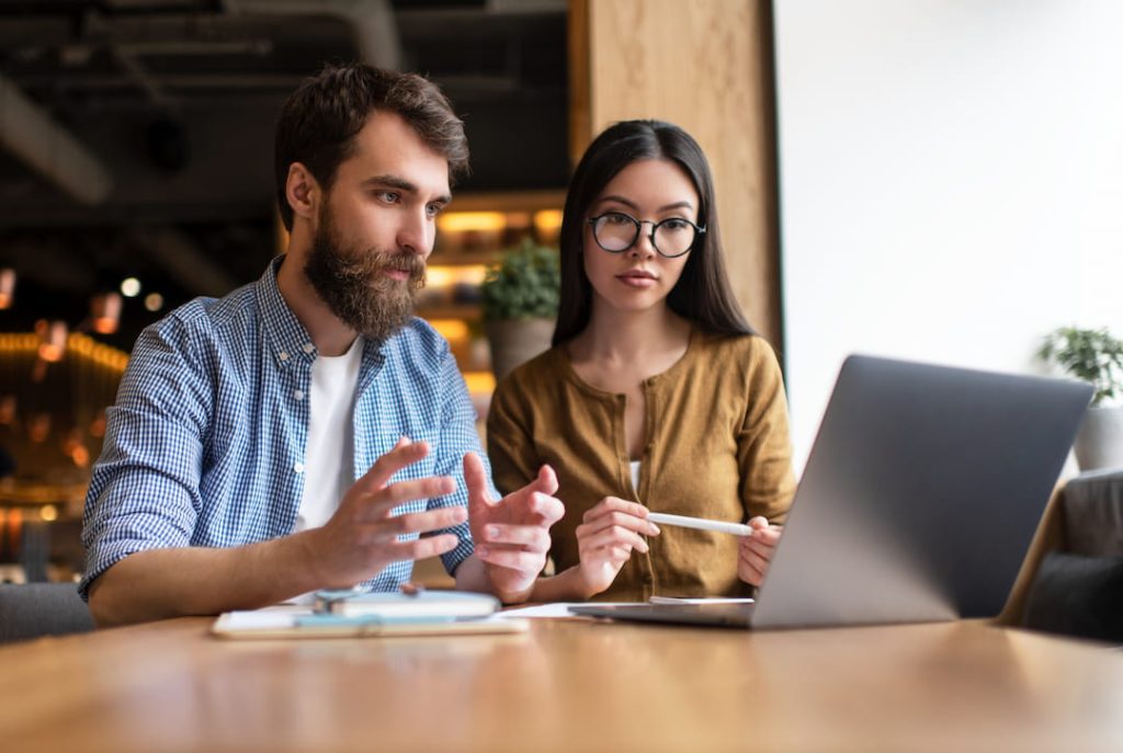 Two coworkers looking at a laptop engaging in an upskilling program in an office with industrial decor