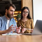 Two coworkers looking at a laptop engaging in an upskilling program in an office with industrial decor