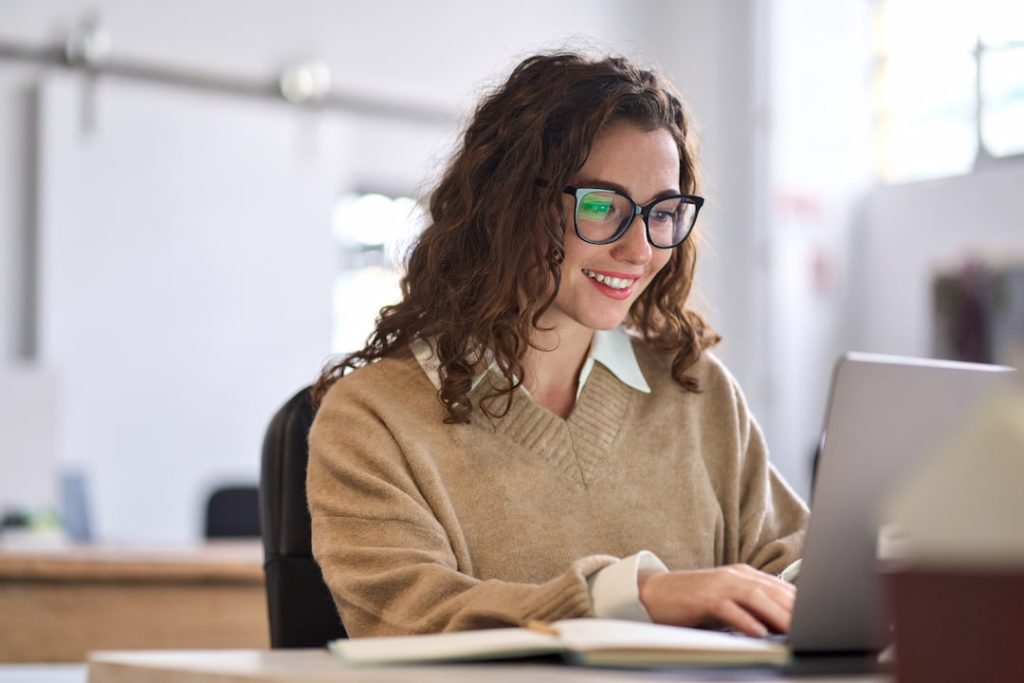 Young female professional working with generative AI in the workplace on her laptop at a desk in a well lit office